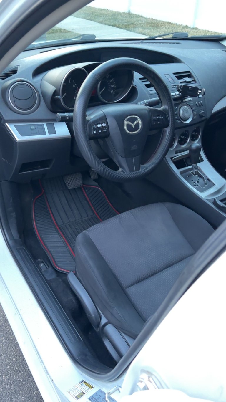 Interior view of a Mazda vehicle showing steering wheel, dashboard, and drivers seat with red and black upholstery