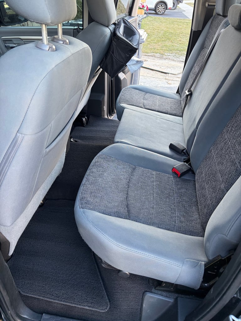 Interior view of a vehicles rear passenger seating area with gray and white upholstered seats and an open door showing the exterior parking lot