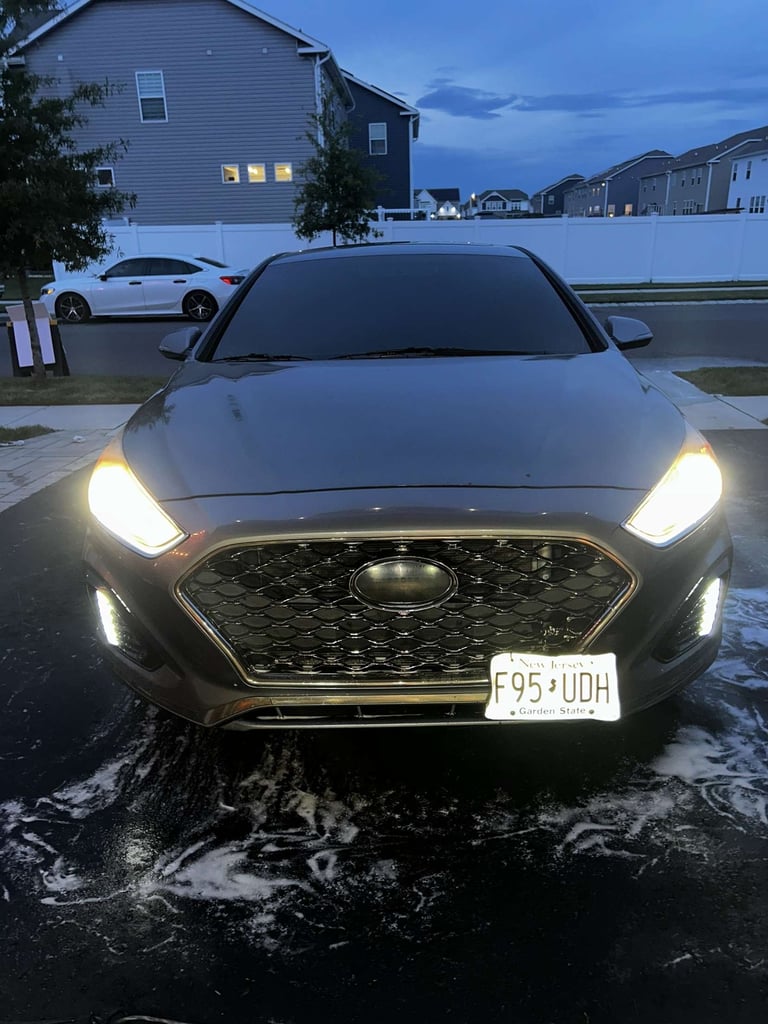 Black Hyundai sedan with LED headlights parked in driveway at dusk, residential neighborhood in background
