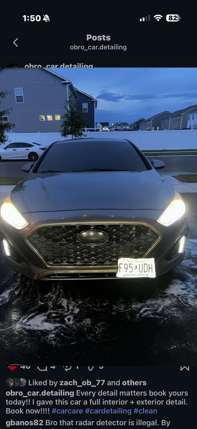 Black sedan with illuminated headlights parked in driveway at dusk, showing detailed car care results from a detailing service