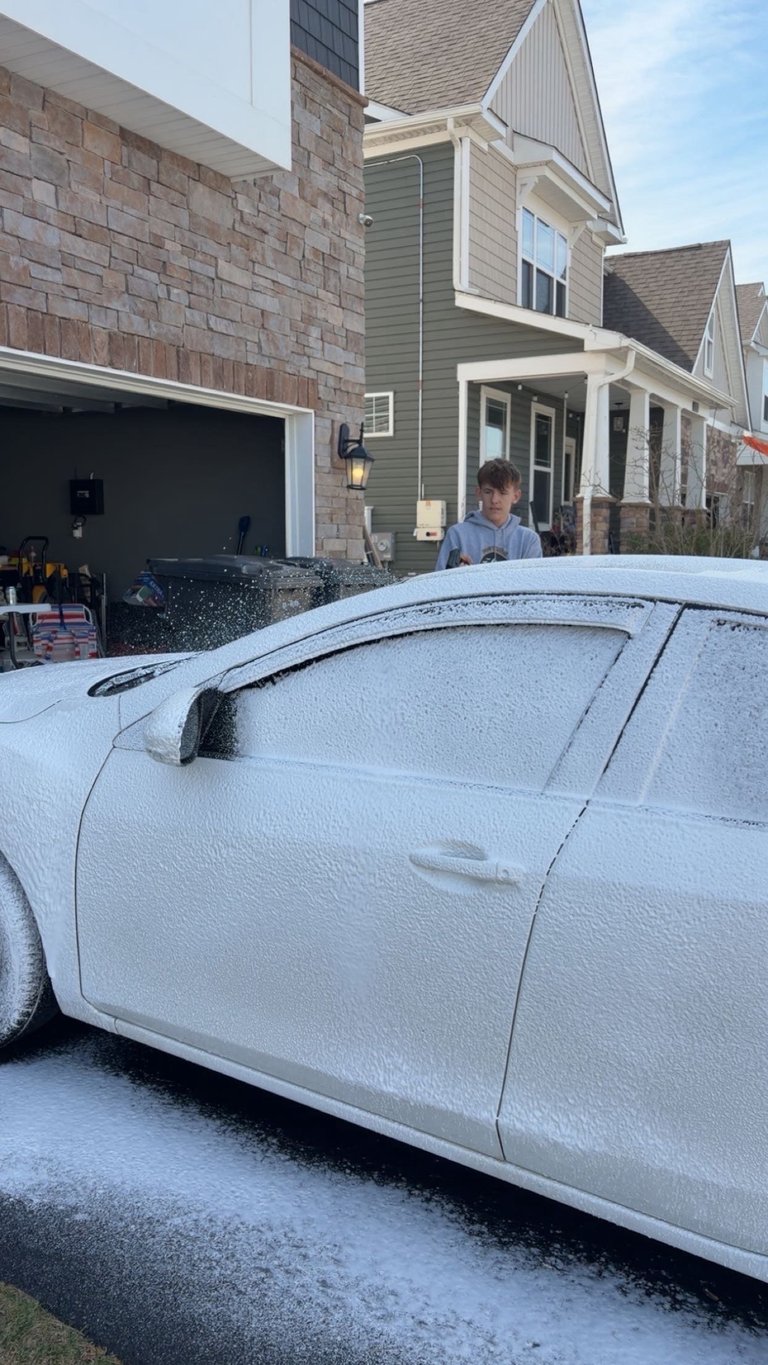 White car covered in frost parked in driveway in front of two-story house with stone and siding exterior